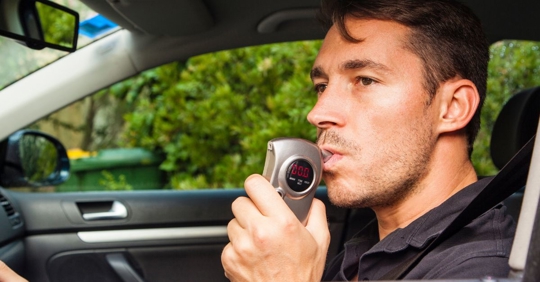 man in car blowing into ignition interlock device